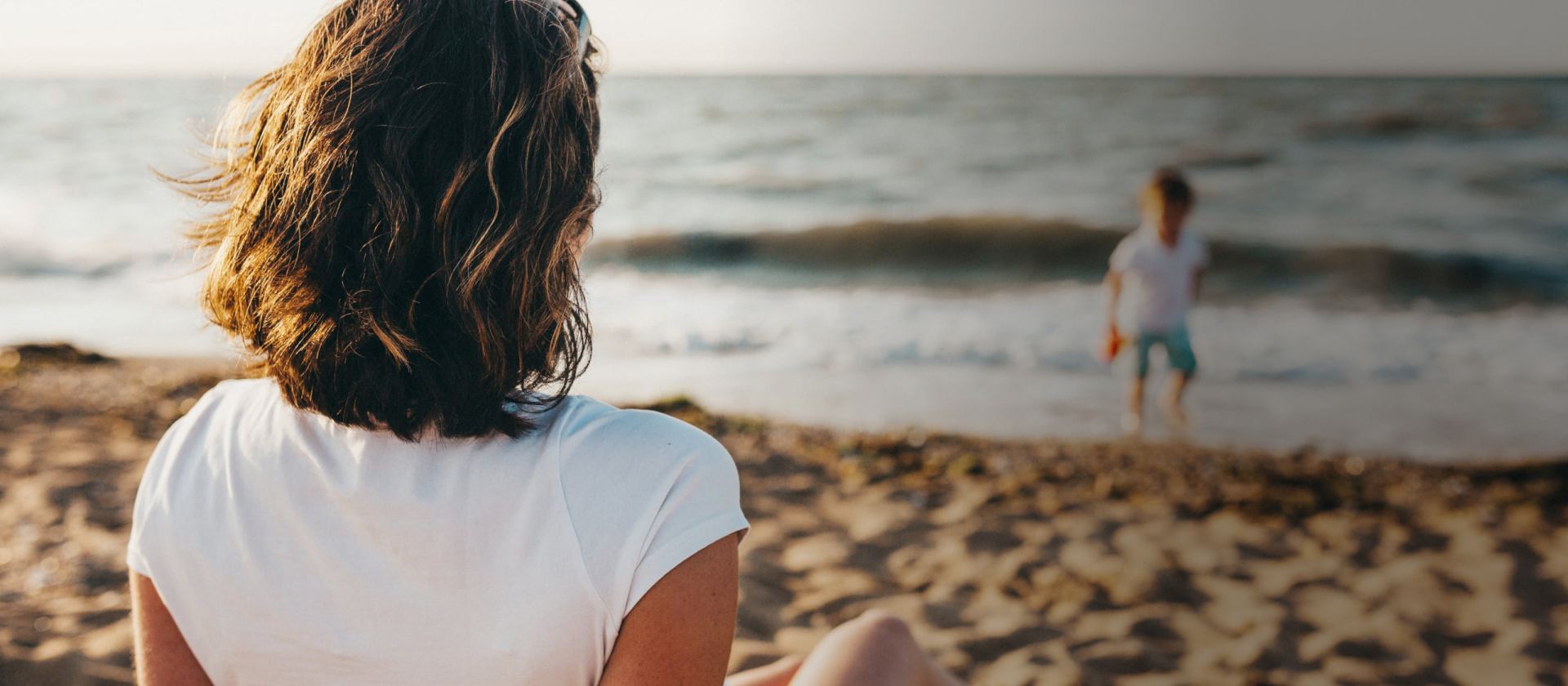A woman watching a child play at the beach